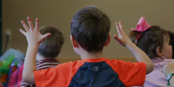 Children at the library sitting on the floor, listening to a storytime session and following along with hand motions.