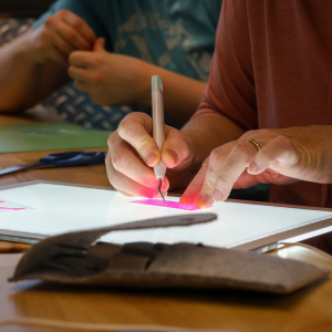 Hands using a pick tool on a project, illuminated by the glow of an iPad screen